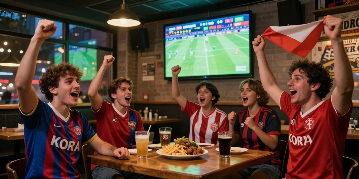 Fans enjoying kora live soccer match in an urban pub, cheering with drinks and flags.